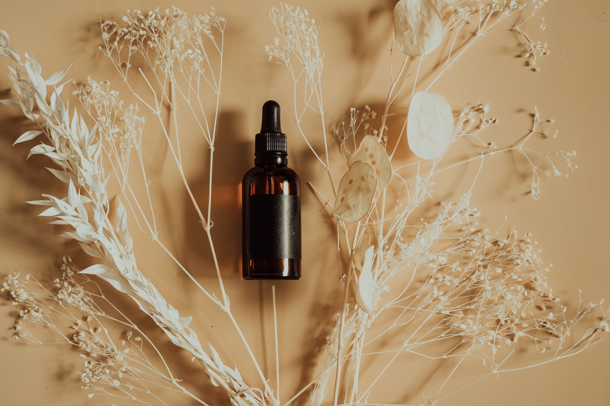Botanical serum dropper bottle surrounded by dried flowers